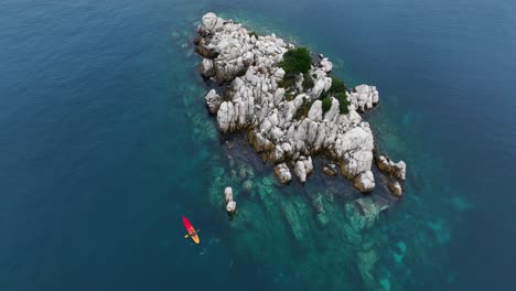 kayak remando cerca de una pequeña isla rocosa en el mar, ángulo alto aéreo