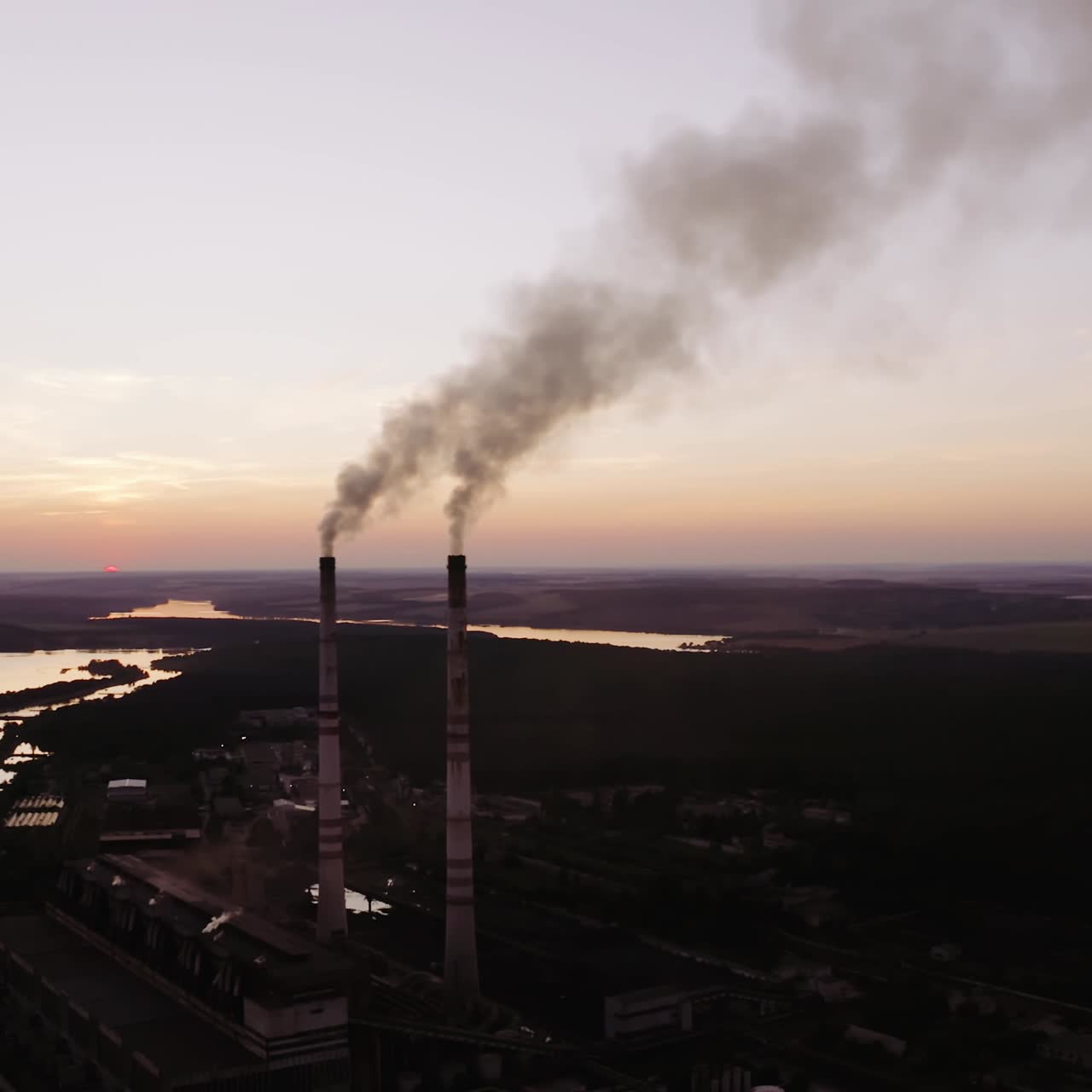 Industrial factory near the river. Harmful smoke comes into the air in the evening. Metallurgical plant produce chemical smoke through pipes.