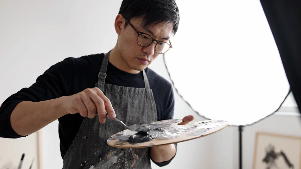 アーティストが木製パレットで慎重に絵の具を混ぜ、柔らかな照明が芸術的な雰囲気を高めるクリエイティブなスタジオ環境で技術を披露する様子
