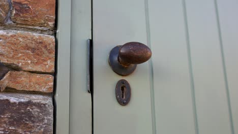 close up of old fashioned brass door handle into a rustic farmhouse building with light painted wooden door and stone work