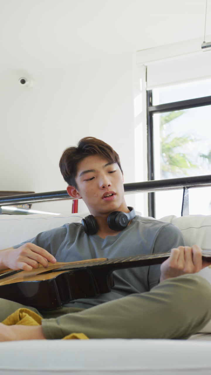 아시안 남성 십대가 거실에서 기타를 연주하는 수직 비디오