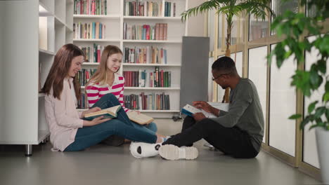 estudiantes felices disfrutan de la lectura de libros humorísticos en la biblioteca. hombre negro coquetea con mujeres bonitas durante la reunión del club de lectores en la librería. ocio intelectual