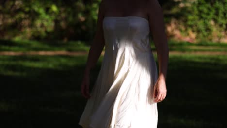 woman with a white strapless summer dress walk slowly outdoors from the shadow into the sun opening her arm in a revealing movement