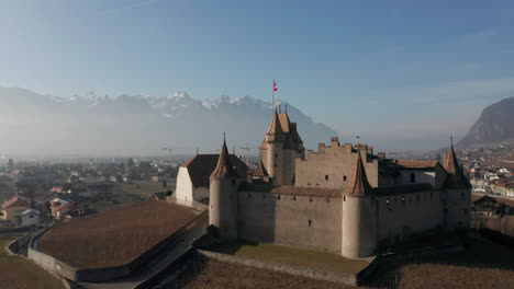 drone flying over beautiful castle with a swiss flag flying on top of tower and revealing the beautiful old town of aigle in switzerland