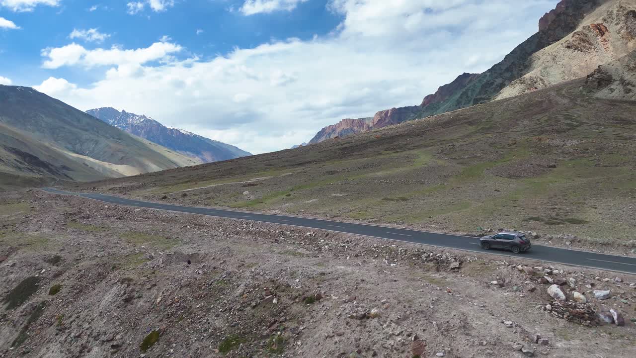 Aerial drone shot of a car driving on a winding yet mostly straight road amidst Ladakh’s arid landscape.