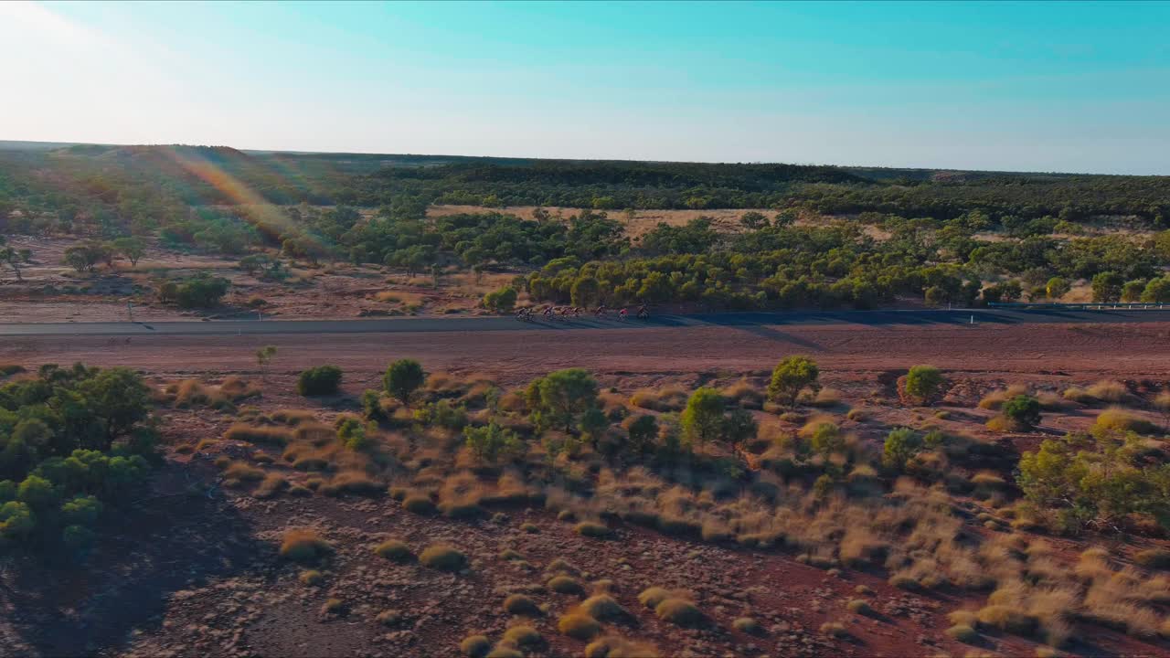 Vista aerea di ciclisti che pedalano in fila su una strada remota nell'entroterra, nel deserto australiano arido e polveroso, in un pomeriggio d'estate