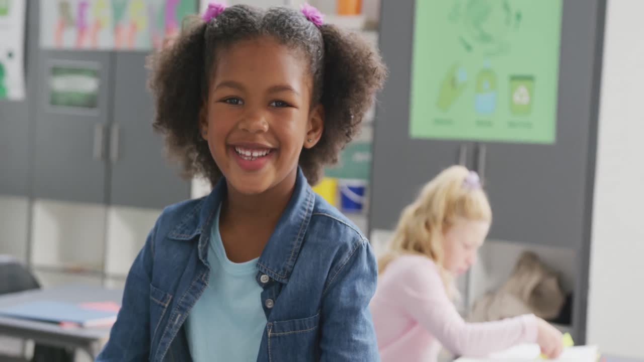 Video portrait of happy biracial schoolgirl smiling in school classroom