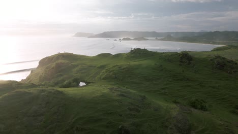 Toma-Aérea-Hacia-Atrás-De-Las-Hermosas-Colinas-De-Bukit-Merese-Rodeadas-Por-El-Océano-índico-Durante-La-Puesta-De-Sol-En-La-Isla-De-Lombok