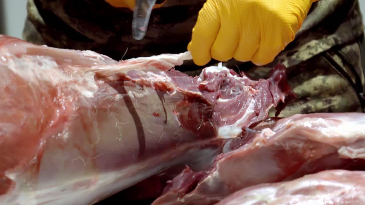 Butcher cutting raw meat wearing yellow gloves in detailed close-up