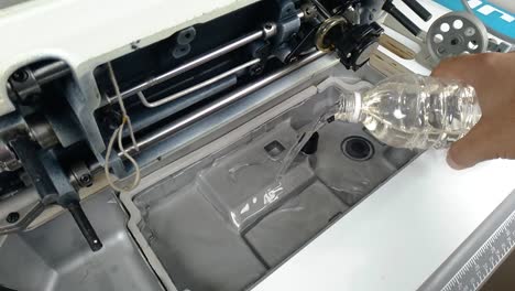 primer plano, las manos a medida vierten aceite de la botella en la máquina de coser, estático