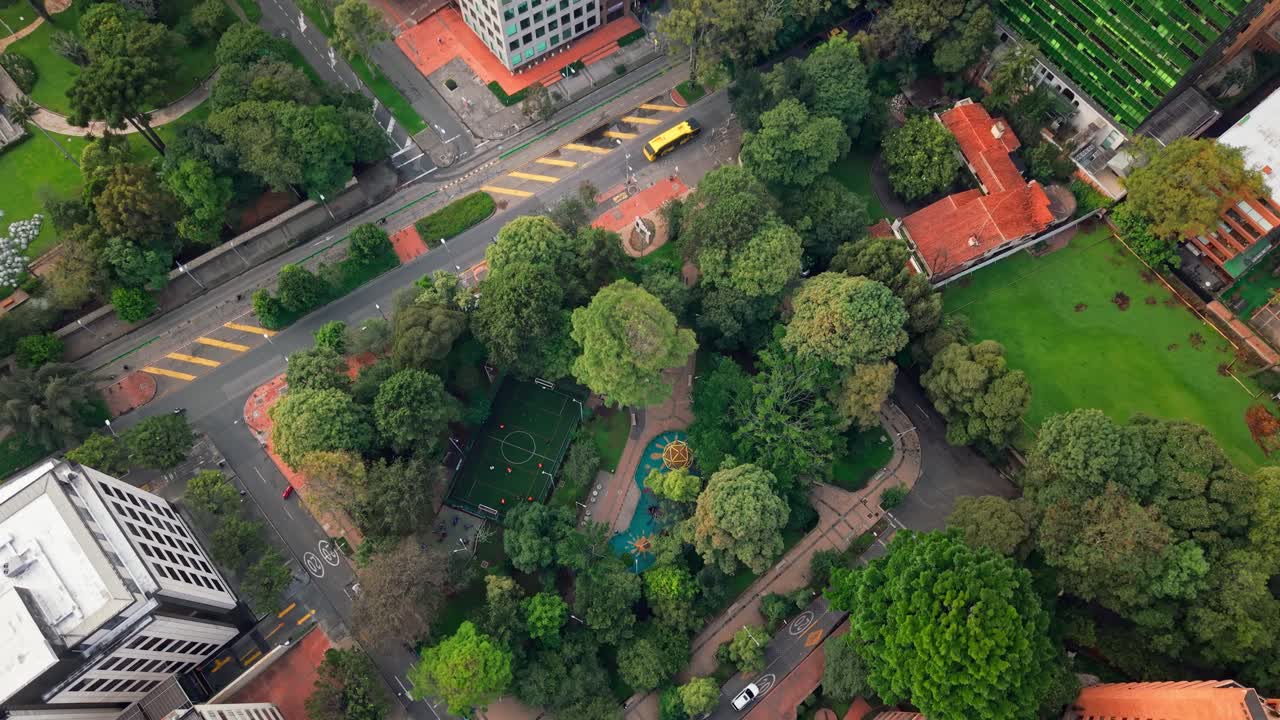 Top-down drone shot of Bogotá showing a football field, buildings, streets, trees, and green areas.