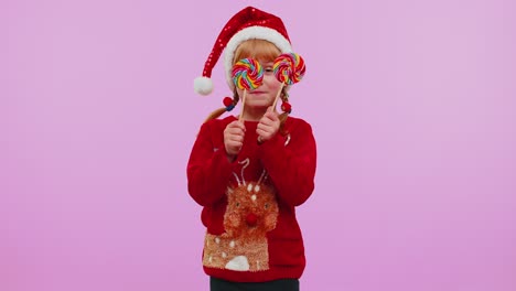 Joyful-girl-in-New-Year-sweater-holding-candy-striped-lollipops-hiding-behind-them,-fooling-around