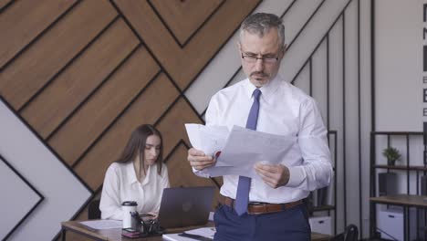 un trabajador está lanzando al aire unos papeles con gráficos. hay otra compañera de trabajo en la oficina.