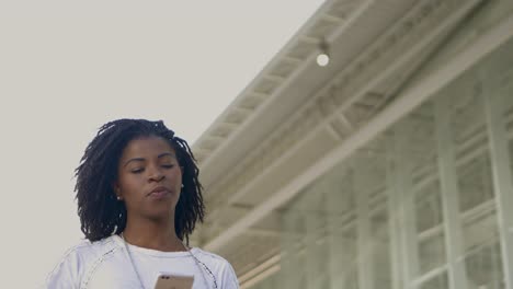 Lächelnde-Afroamerikanische-Frau,-Die-Beim-Spaziergang-Ihr-Smartphone-Benutzt.