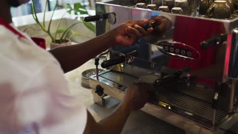 Mittelteil-Eines-Afroamerikanischen-Männlichen-Barista,-Der-Kaffee-In-Der-Kaffeemaschine-Zubereitet