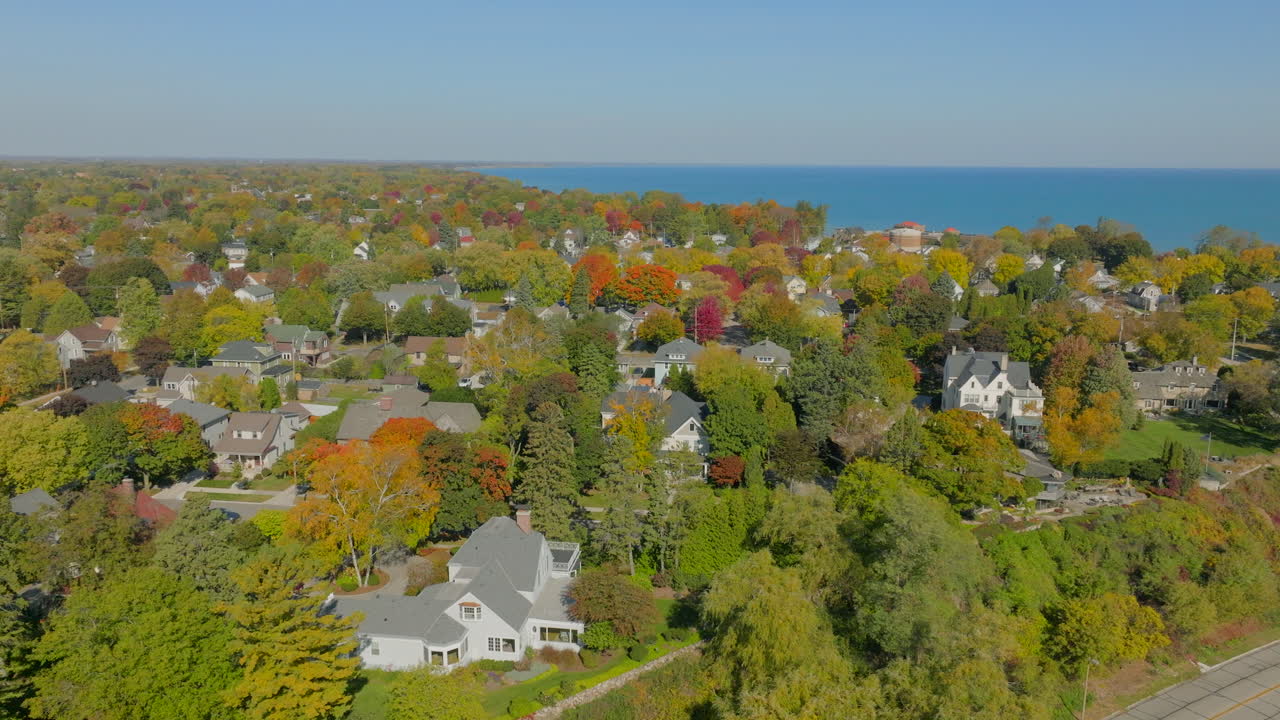 Drone aerial panning over Sheboygan, Wisconsin neighborhood homes and autumn trees with Lake Michigan on the horizon under a clear, pretty blue sky