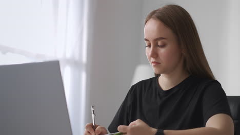 Studentin-Lernt-Online-Zu-Hause-Und-Sieht-Sich-Webinare-Und-Vorlesungen-Auf-Dem-Bildschirm-Eines-Laptops-Mit-Internet-An,-Macht-Sich-Notizen,-Porträt-Einer-Frau-Im-Innenbereich