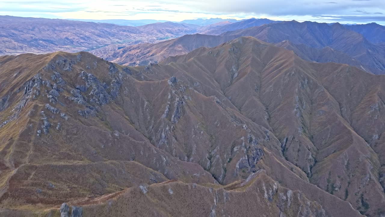 Drone flies forward over rugged mountain ridges of Roys Peak, revealing the distant valleys and surrounding alpine landscape