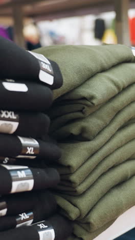 vista de ropa bien plegada en varios colores con etiquetas de tamaño (s, m, l, xl, xxl) exhibida en los estantes de un centro comercial. capturada con una cámara de mano, haciendo hincapié en el entorno minorista organizado
