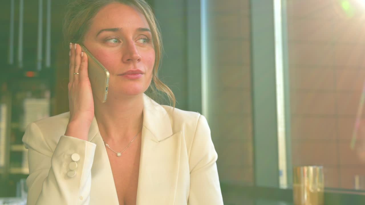 Donna con blazer bianco che parla al telefono in un ristorante