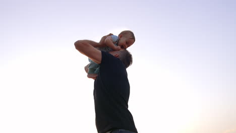 caring father rising his son into air and kissing his little tummy. daddy tossing his baby boy up. low angle view.