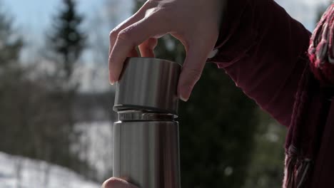 manos de mujer abriendo termo y bebiendo bebida caliente en el bosque de invierno al aire libre