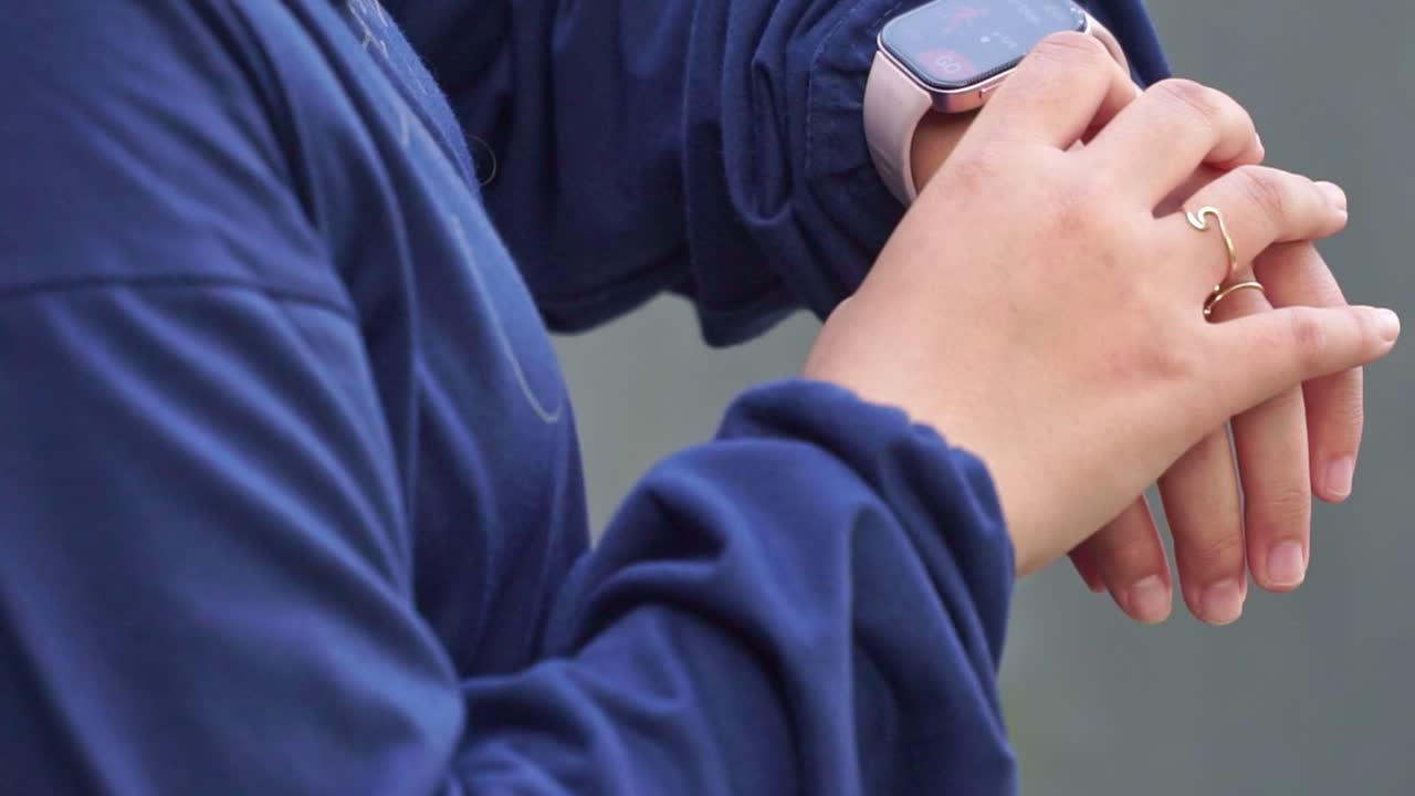 Hand close-up of a woman tapping on a smartwatch screen, showcasing modern wearable technology and touch interface on a casual outdoor setting