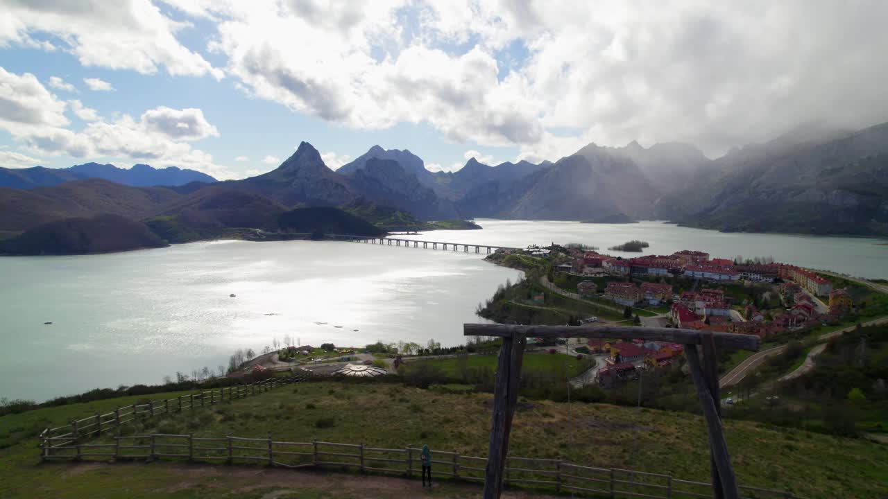 Fast aerial dolly shot with a family swinging their child on the swing at the viewpoint in Ria&ntilde;o, a village in Le&oacute;n, Spain on the shore of a large reservoir in the Cantabrian mountains