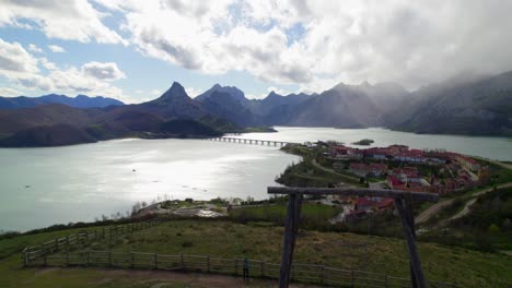 Fast-aerial-dolly-shot-with-a-family-swinging-their-child-on-the-swing-at-the-viewpoint-in-Riaño,-a-village-in-León,-Spain-on-the-shore-of-a-large-reservoir-in-the-Cantabrian-mountains