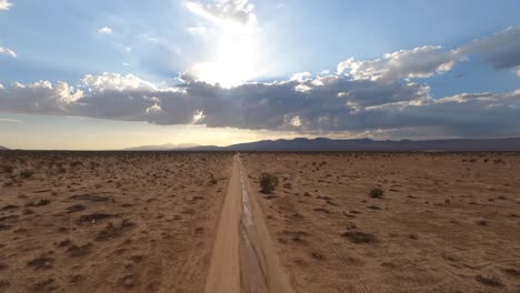 volando sobre un camino de tierra a través del desierto de mojave hacia las montañas y la puesta del sol - vuelo rápido en primera persona