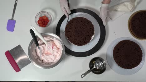 front shot of a baker using an icing spatula to carefully touch up sides of cream covered cake.