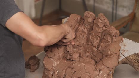 a top view of a male potter shaping clay to make ceramic sculpture of human hand using professional tool. stylish interior art studio on blurred background