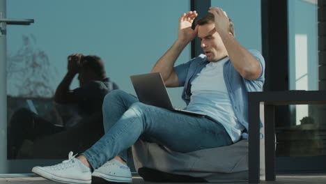 upset man working on laptop. worried specialist sitting with notebook outdoor