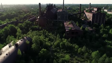 aerial view of overgrown abandoned industrial complex in a lush green landscape, showcasing nature's reclamation of a once-bustling manufacturing site