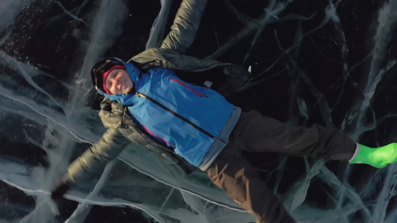 el dron gira y se aleja. una niña yace en el hielo en invierno, agitando sus brazos y piernas hacia un lado, representando a un ángel.