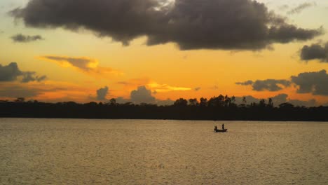 a boat glides along the river at sunset, with twilight and orange clouds overhead, in a serene fishing scene in bangladesh