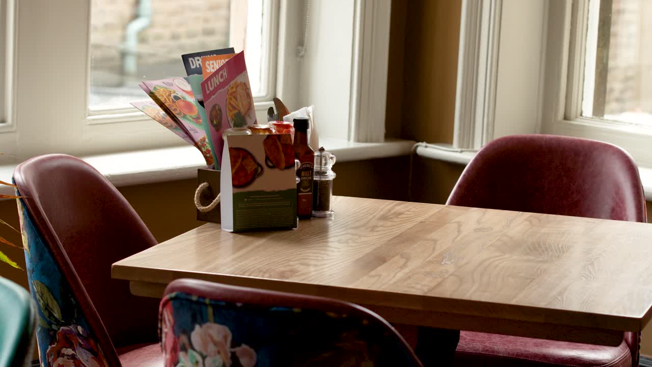 Natural light illuminates retro cafe table, leather chairs, and condiments during smooth camera pan
