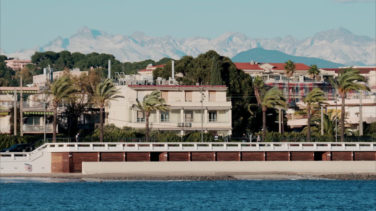Buildings and palm trees on the shore with a view of the mountains in the background in Antibes, France