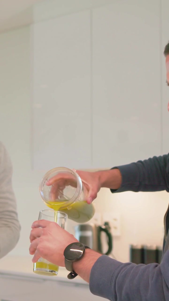 Video vertical: Mezcla lista, hombre con sudadera con capucha cerrando la tapa y sirviendo jugo en un vaso en la cocina, con espacio para texto.