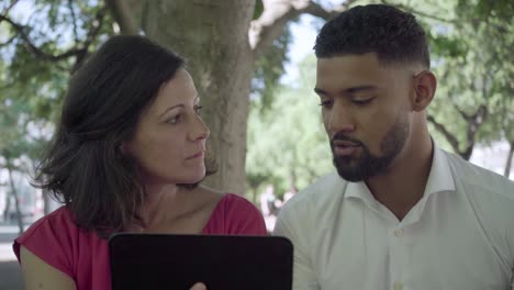 Focused-employees-looking-at-tablet-and-talking-outdoor.