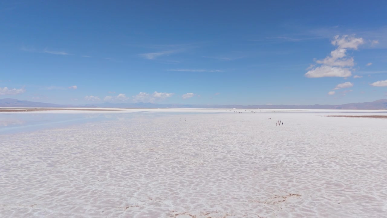 Extensas salinas de Salinas Grandes sob céu azul claro, paisagem aérea minimalista com turistas a passear