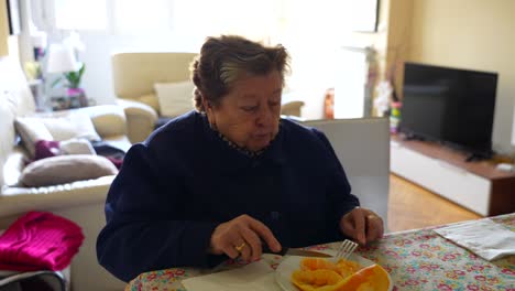 toma de gran ángulo de una anciana comiendo frutas de naranja en casa, sala de estar