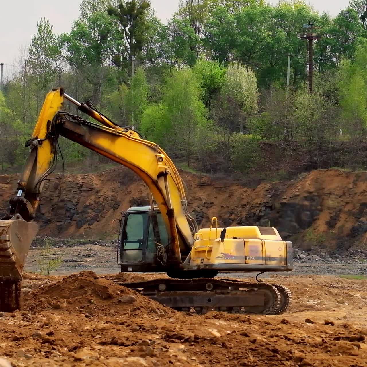 Earth moving equipment. Yellow excavator digging the ground. Excavator bucket scoops up the soil on nature background. Slow motion.