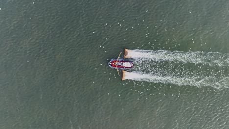 drone topdown shot of a fishers boat dragging the nets thru the water