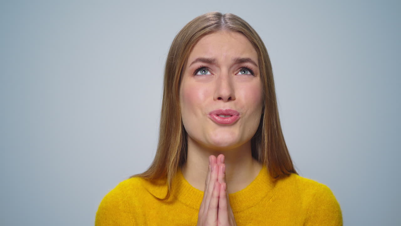 Portrait of young woman showing prayer position with hands on grey background.