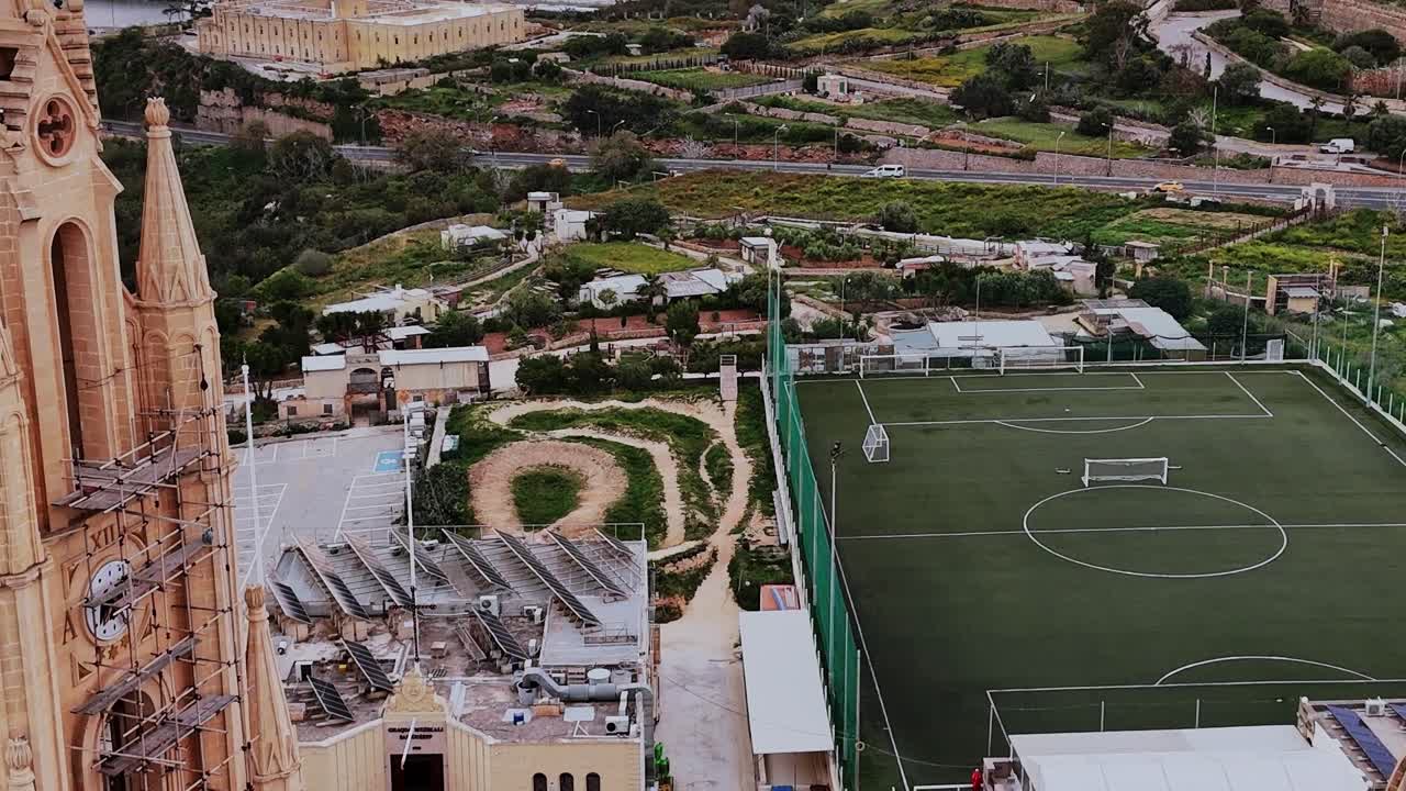 Sports field in Malta with buildings and green hills in background