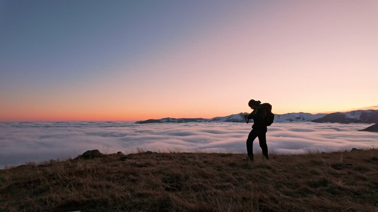 Hiker enjoys a serene sunset above clouds, capturing a peaceful moment
