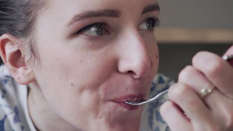 Cute-young-woman-is-eating-a-piece-of-cake-with-a-fork,-smiling-and-looking-to-the-camera