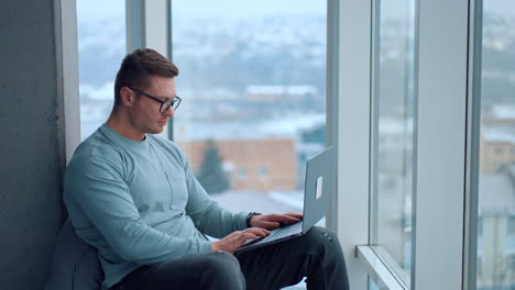 man working on laptop at home office window