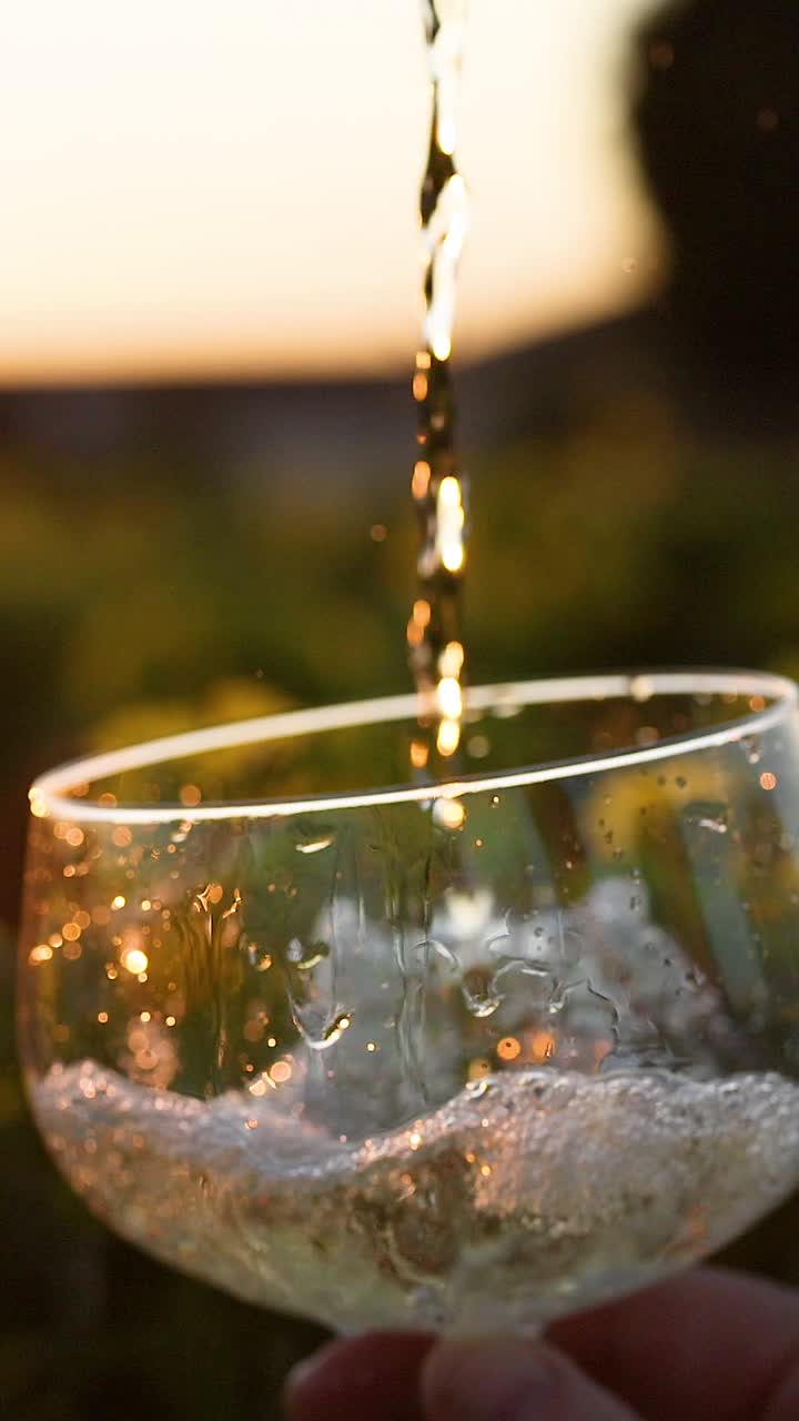 Un primo piano verticale di vino bianco che viene versato in un bicchiere durante il tramonto.
